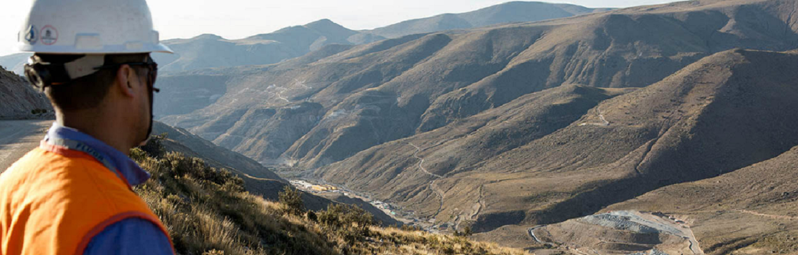 A miner in a hard hat looks out over a copper mine project in the mountains of Chile.