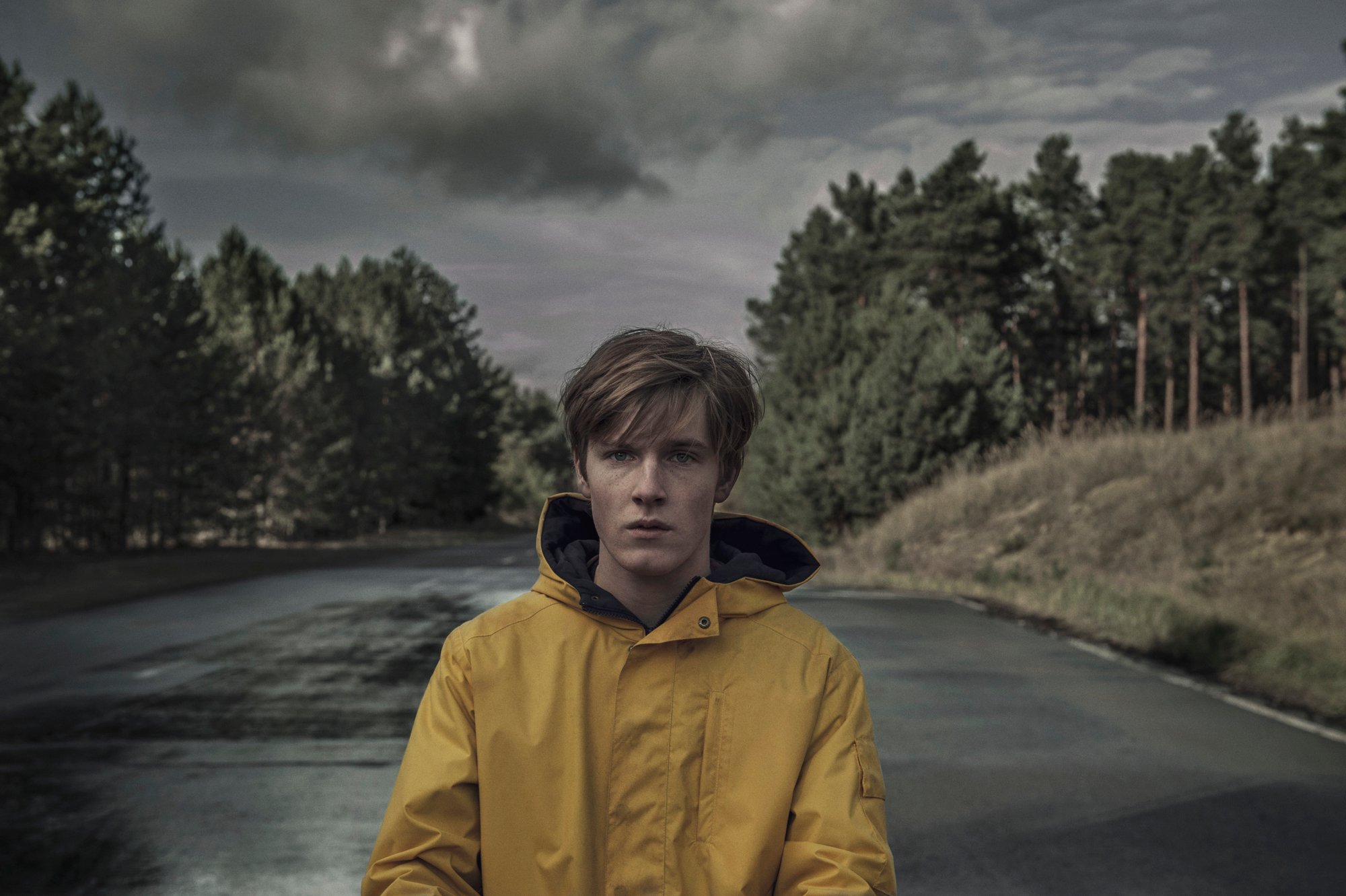 A person standing on a road in a yellow raincoat in a scene from Netflix original Dark.