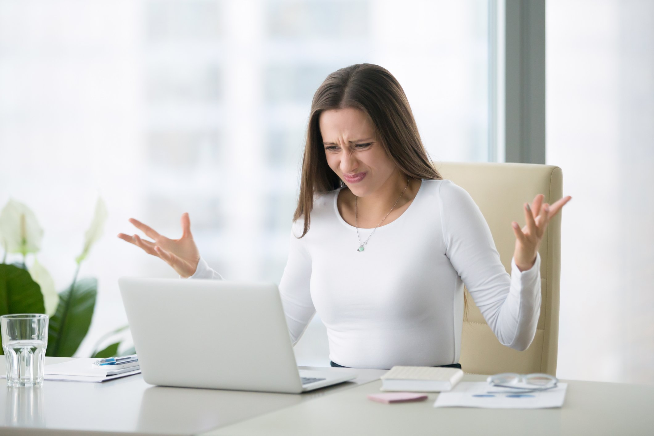 Woman gesturing and staring at laptop screen with disgusted expression.