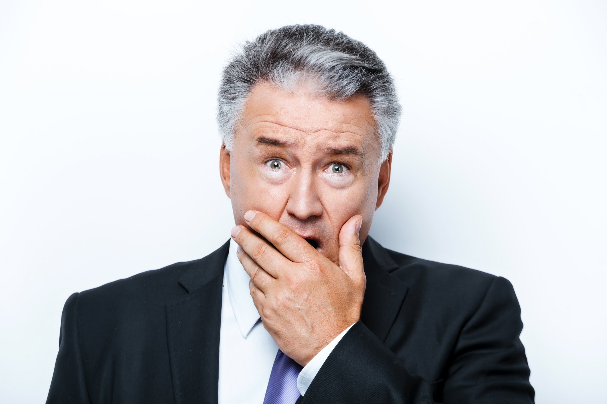 A visibly surprised mature man in a suit, with his hand covering his mouth.