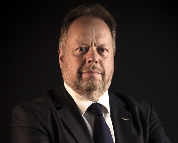 Palmer is shown wearing jacket and tie, seated before a black backdrop.