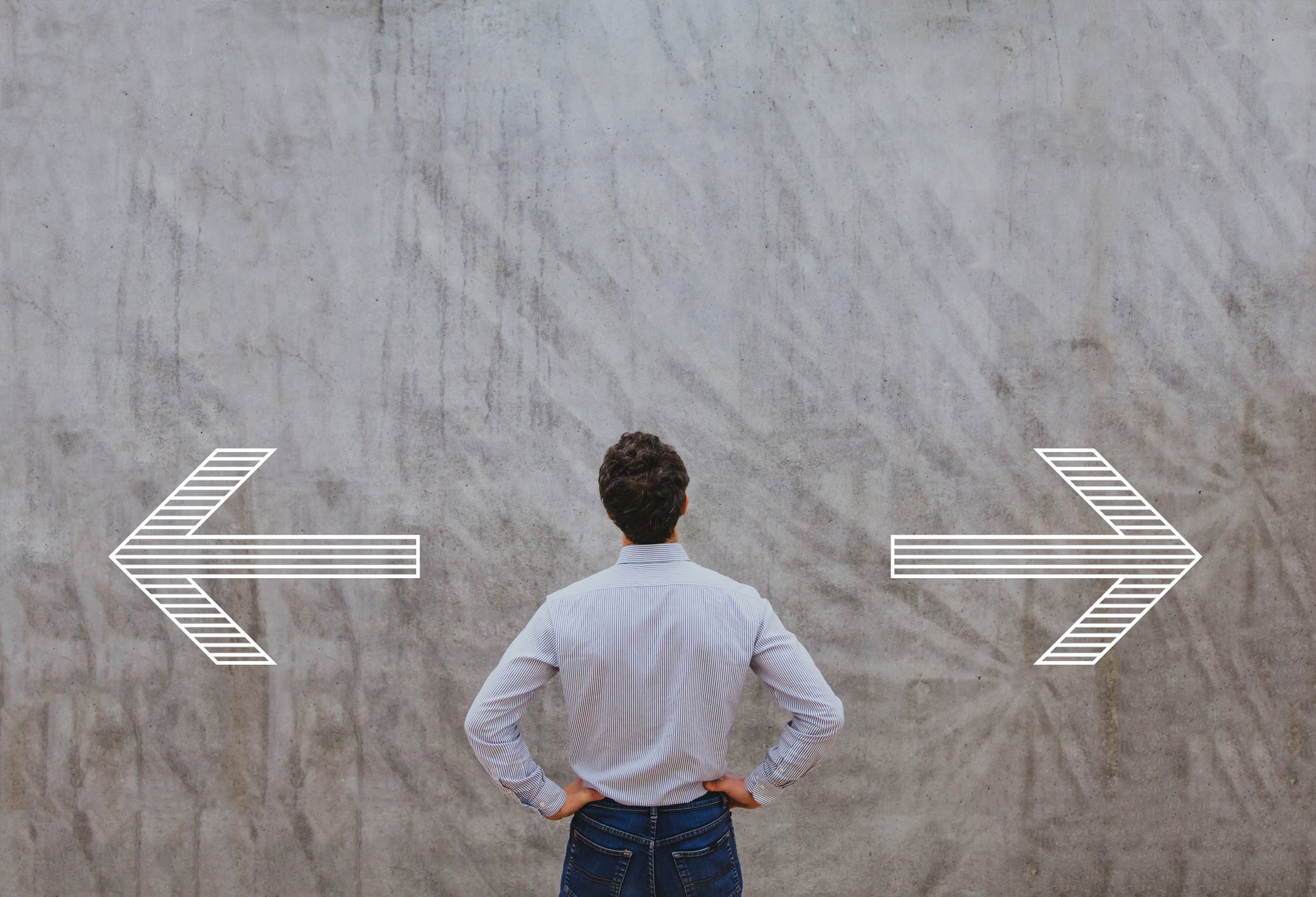 Man with hands on hips looking at arrows on a wall pointing left and right.
