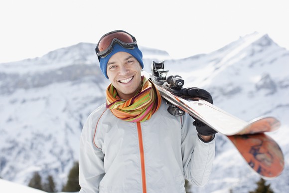 A man smiling while holding skis.