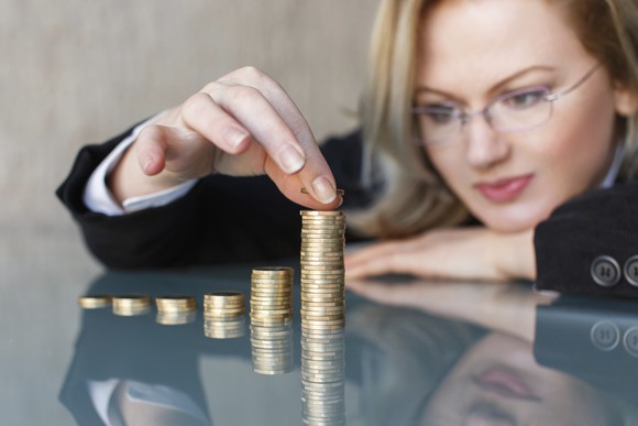 Woman wearing glasses and a business outfit stacking piles of coins on a glass tabletop.