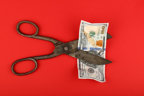 Scissors cutting a $100 bill.