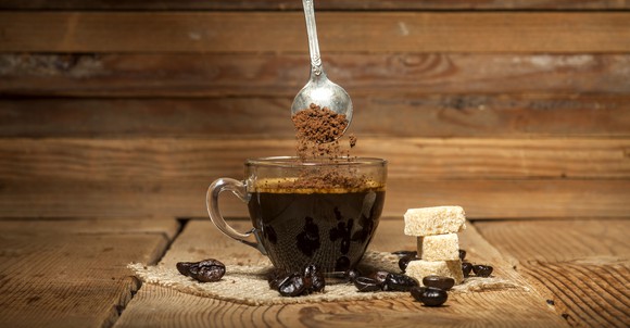 A spoon stirs coffee on a wooden countertop