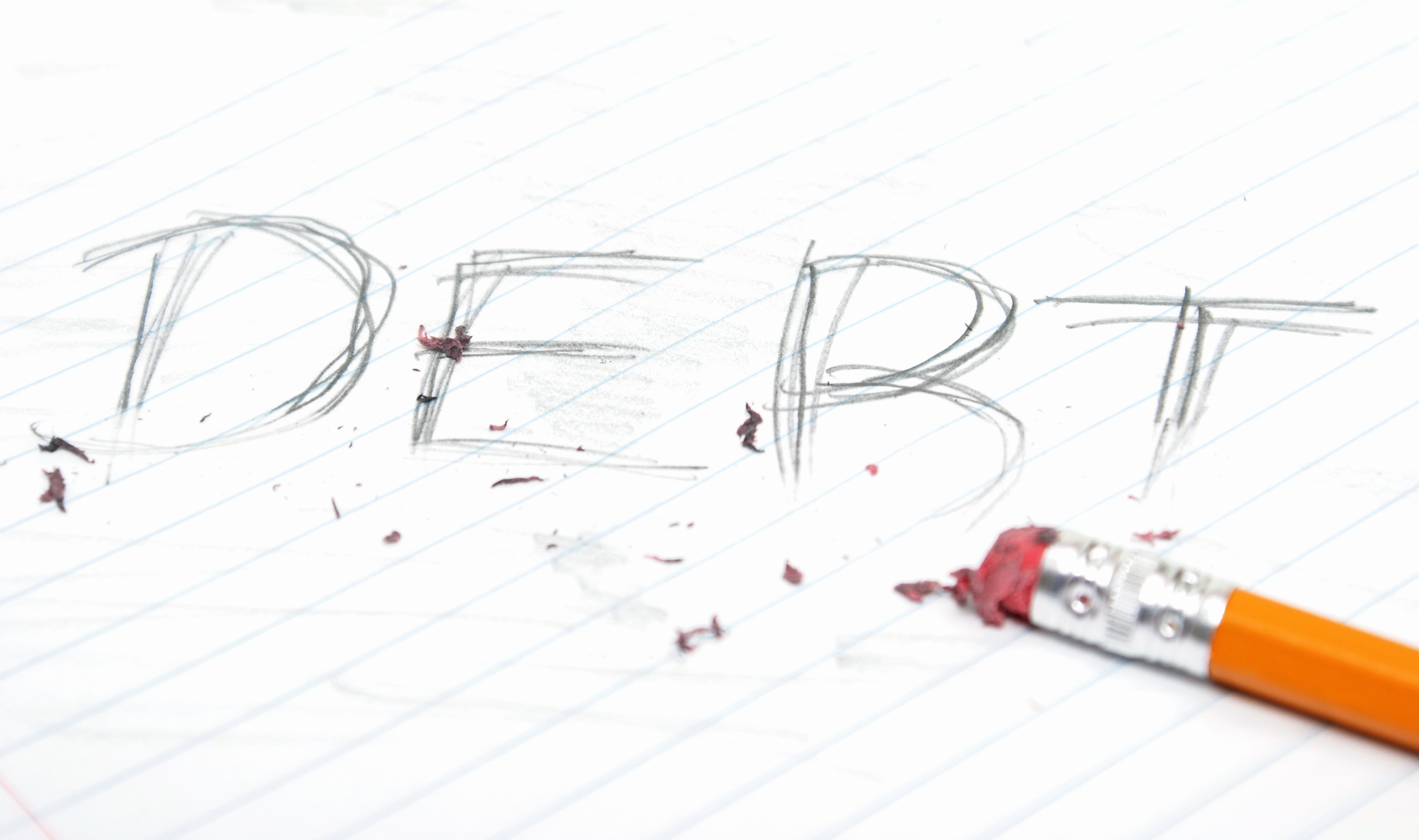 The word "debt" written on lined paper, half erased by a pencil, some of which is visible.