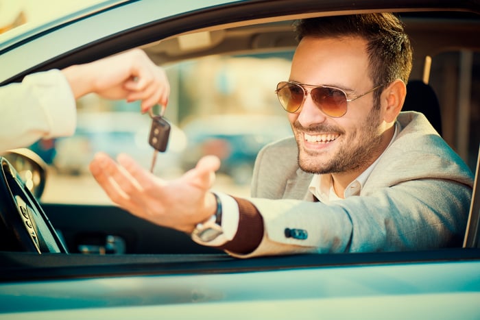 A smiling man receives the key to his new car.