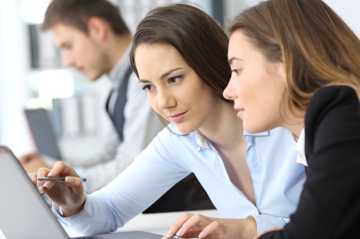 One woman helps another in an office.