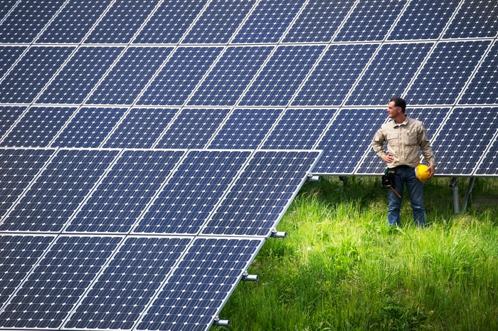 Worker at solar farm looking at solar panels while holding a yellow hard hat.