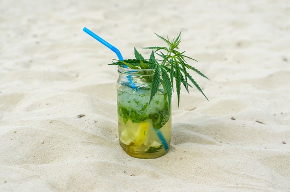 A drink in the sand with a marijuana leaf in it.