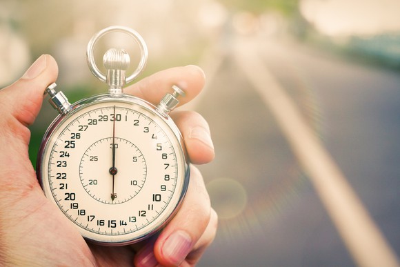 Close-up of hand holding antique stopwatch before a blurred road background.