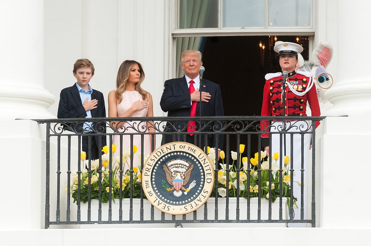 President Trump with his right hand over his heart during the singing of the national anthem, flanked by his wife Melania, and his son Barron. 
