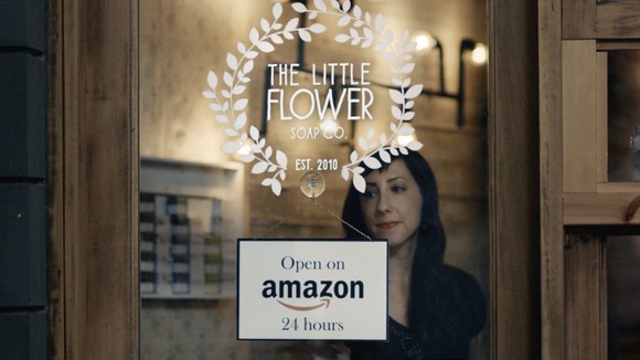 A woman stands in front of a sign touting that her store is open 24 hours on Amazon.