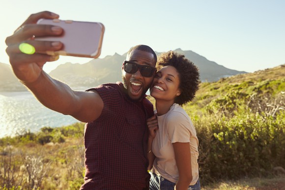 Couple taking a selfie with a body of water and a mountain in the background