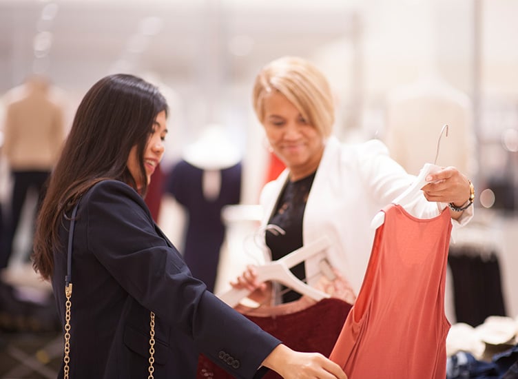 A woman holds up a blouse while another woman looks at it.