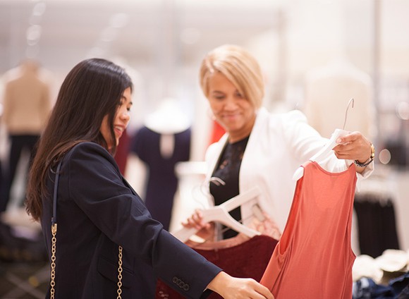 A woman holds up a blouse while another woman looks at it.