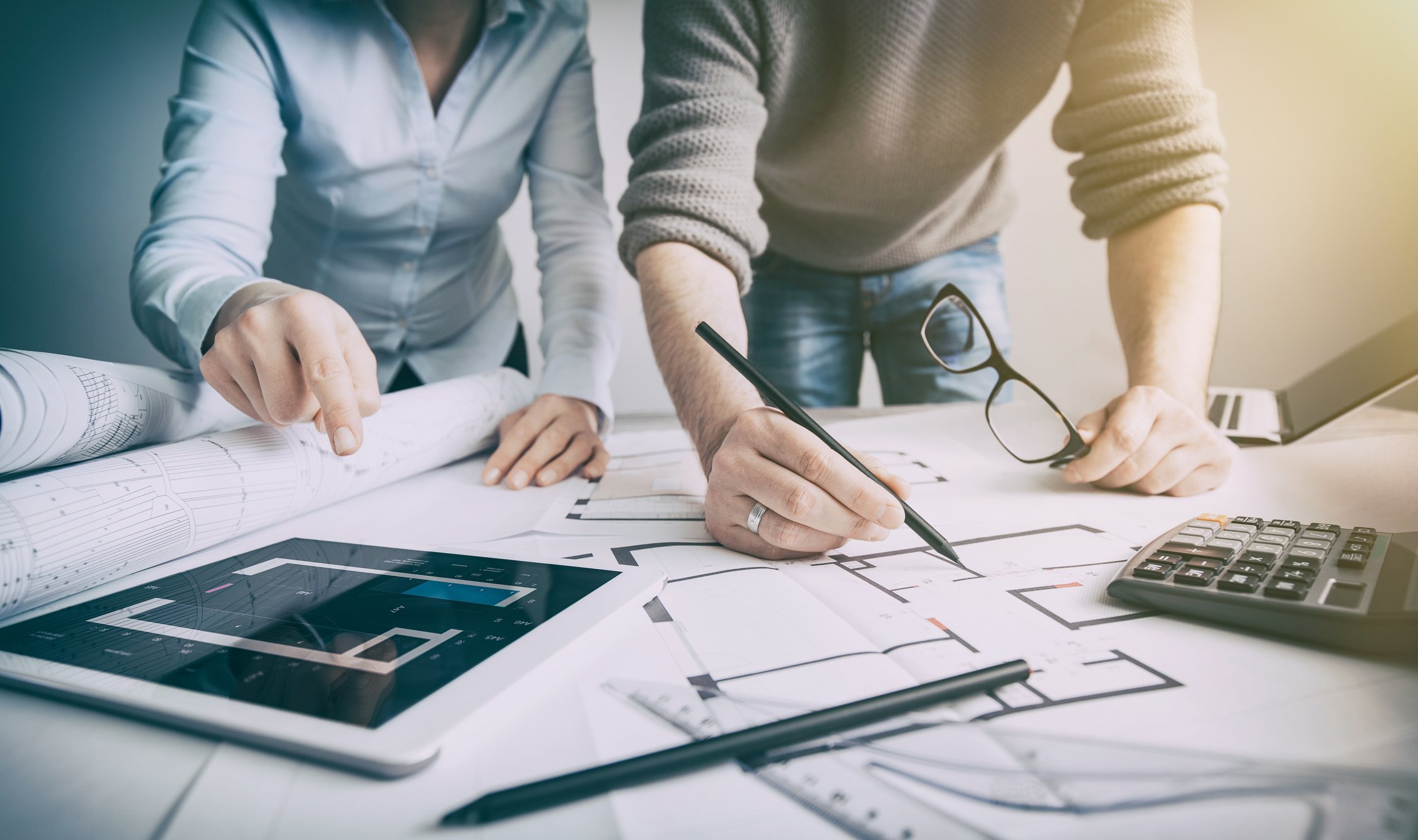 Man and woman with blueprints, tablet, laptop, and calculator, planning home construction