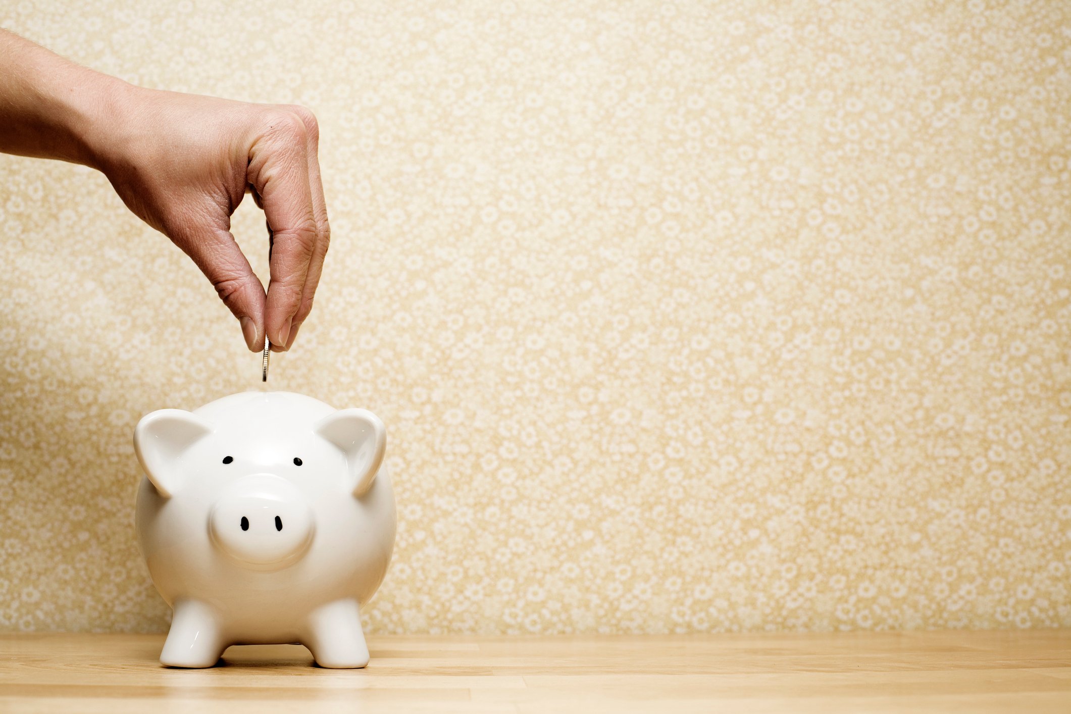 Person dropping a coin into a white piggy bank