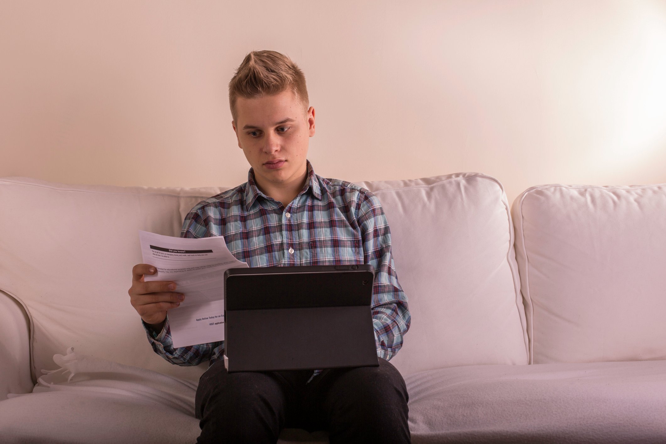 Young male at laptop holding a document.