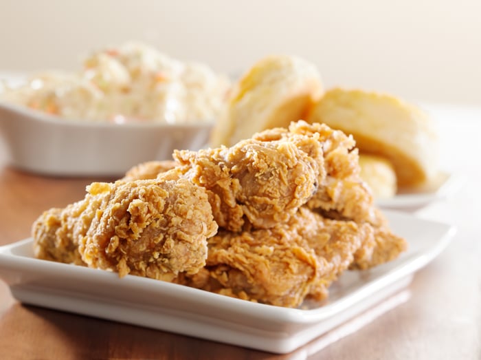 A handful of fried chicken pieces with biscuits on the side.