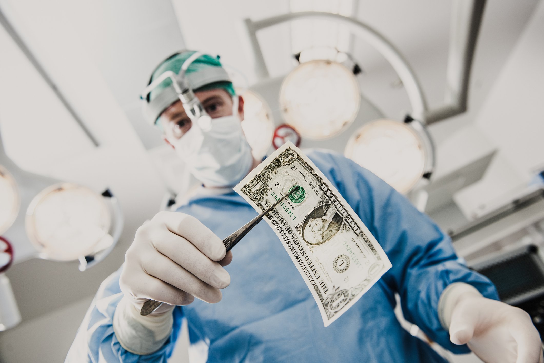 An upward-looking view of a surgeon holding a dollar bill in a pair of forceps.