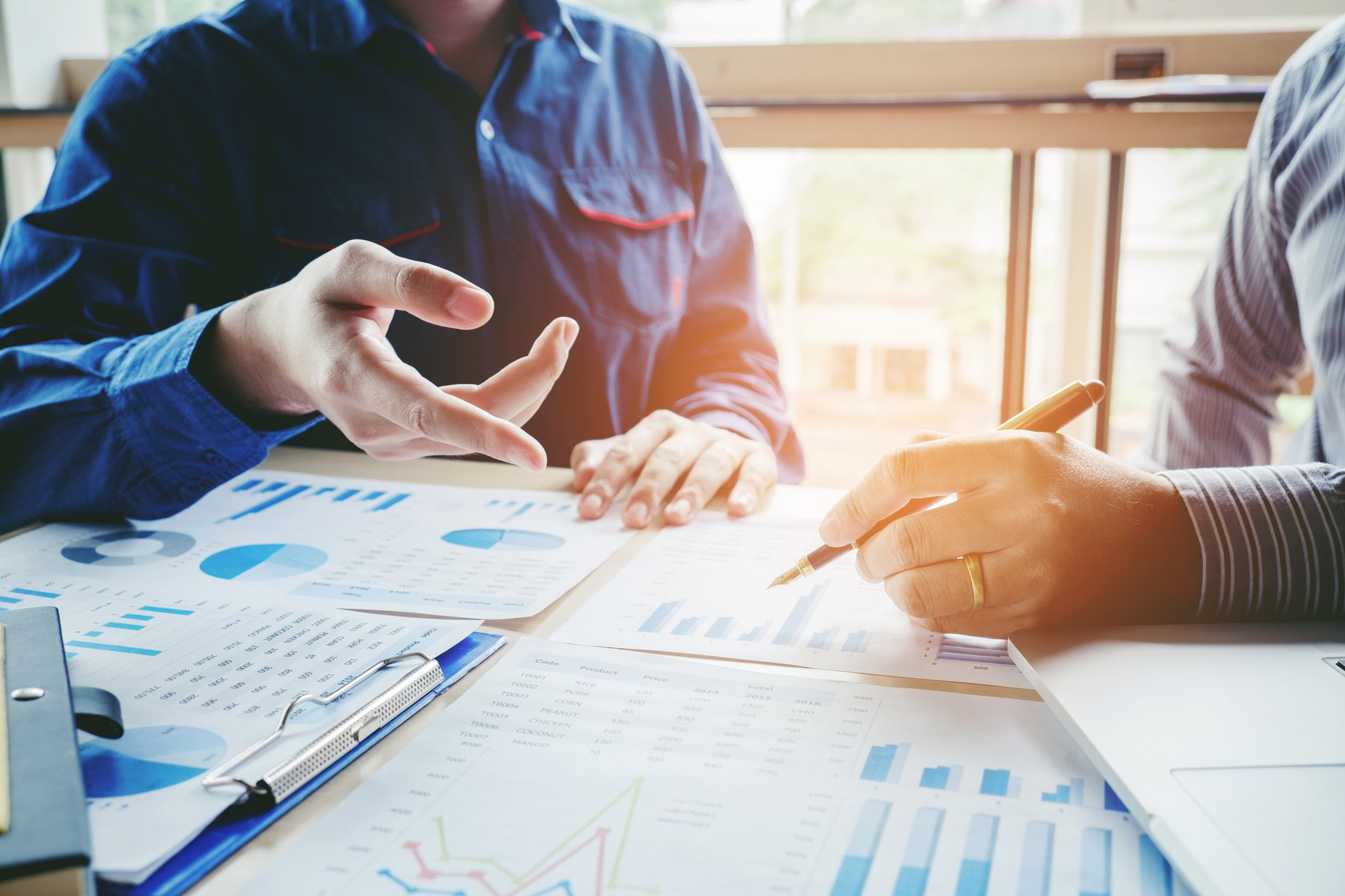 Two men seated facing each other, with various charts on a table in front of them.
