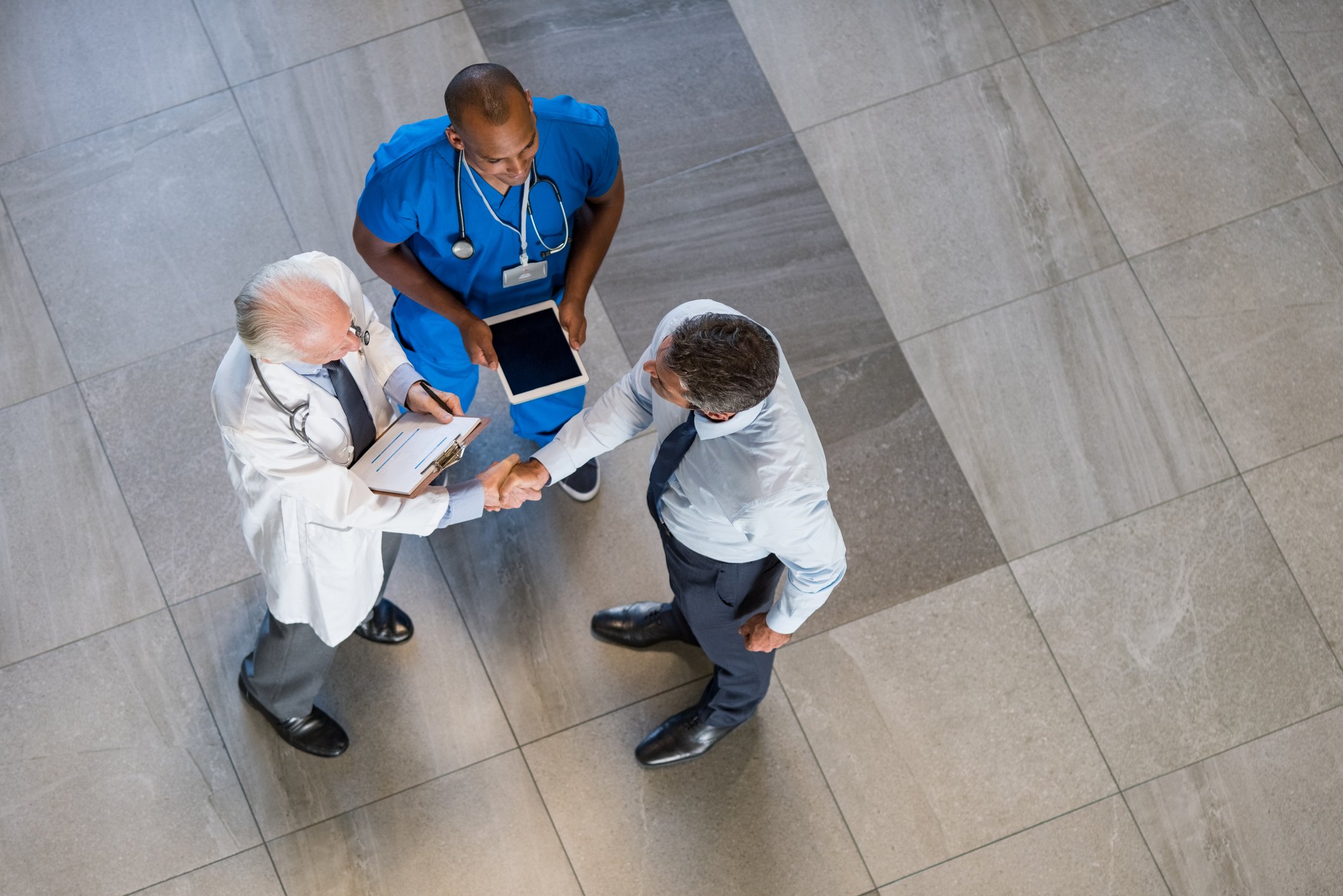 A doctor and a nurse talk with someone in a suit.