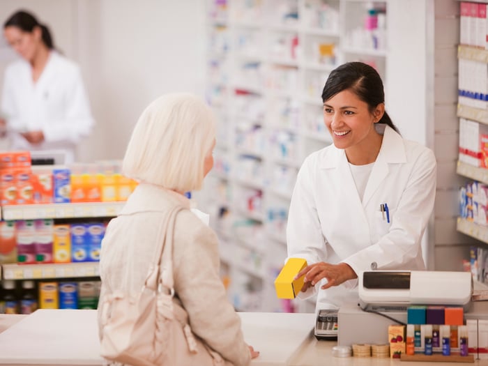 A pharmacist hands medication to another person.