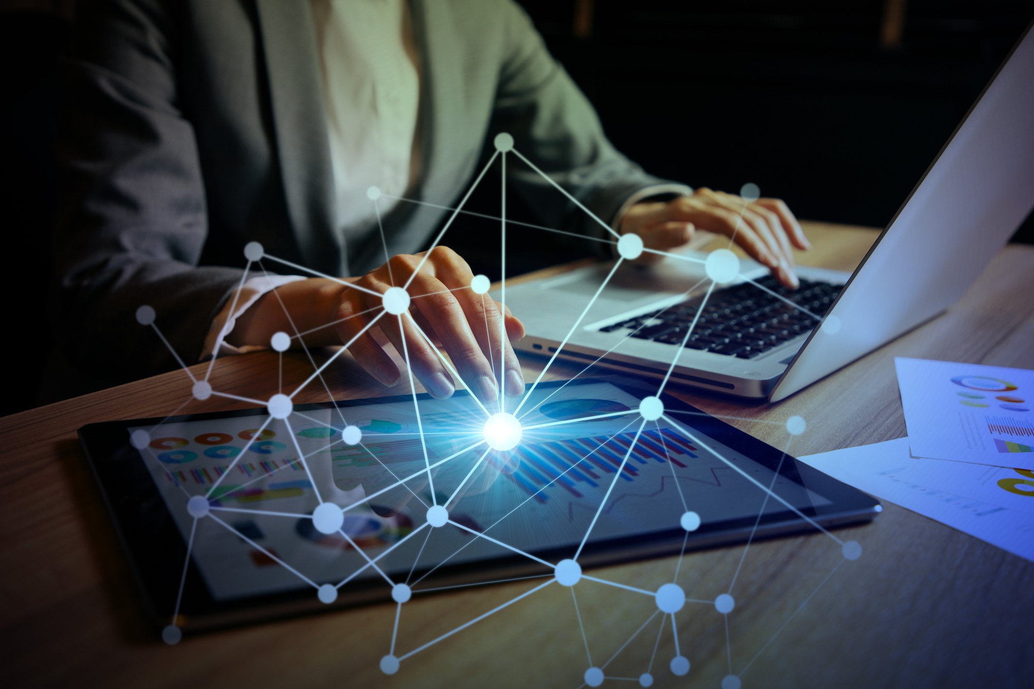 A person using a laptop and a tablet, connected by a web of dots.