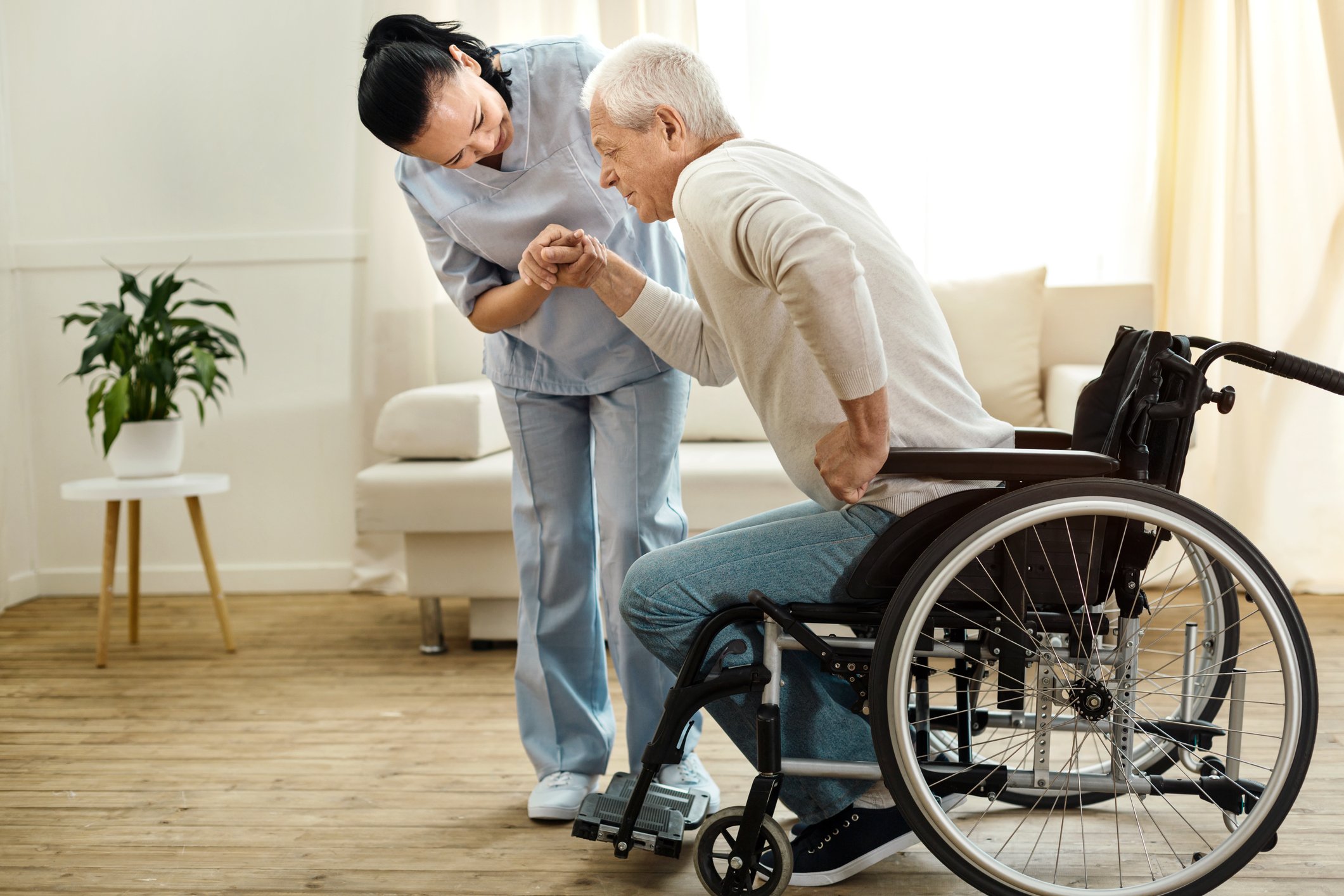 Woman in scrubs helping senior man out of wheelchair.