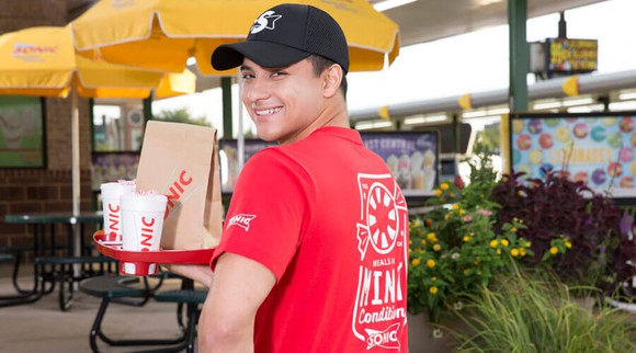 A Sonic carhop smiling while delivering a meal on a tray.