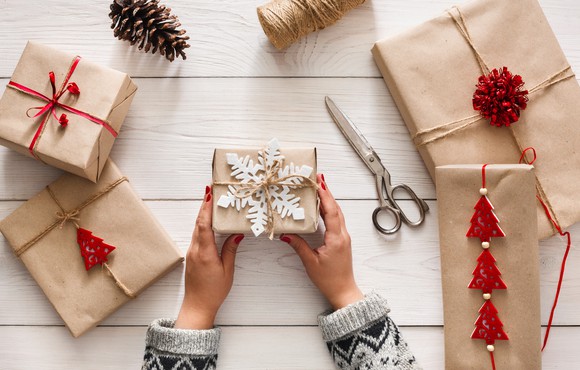 Woman holding a wrapped gift with other wrapped gifts and scissors spread out near her