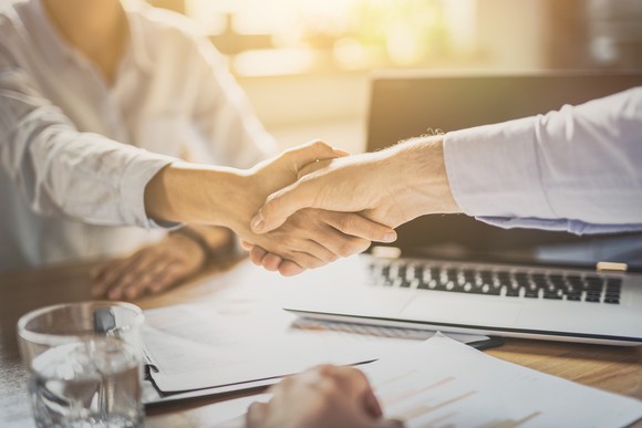 Two businessmen shake hands over a desk.