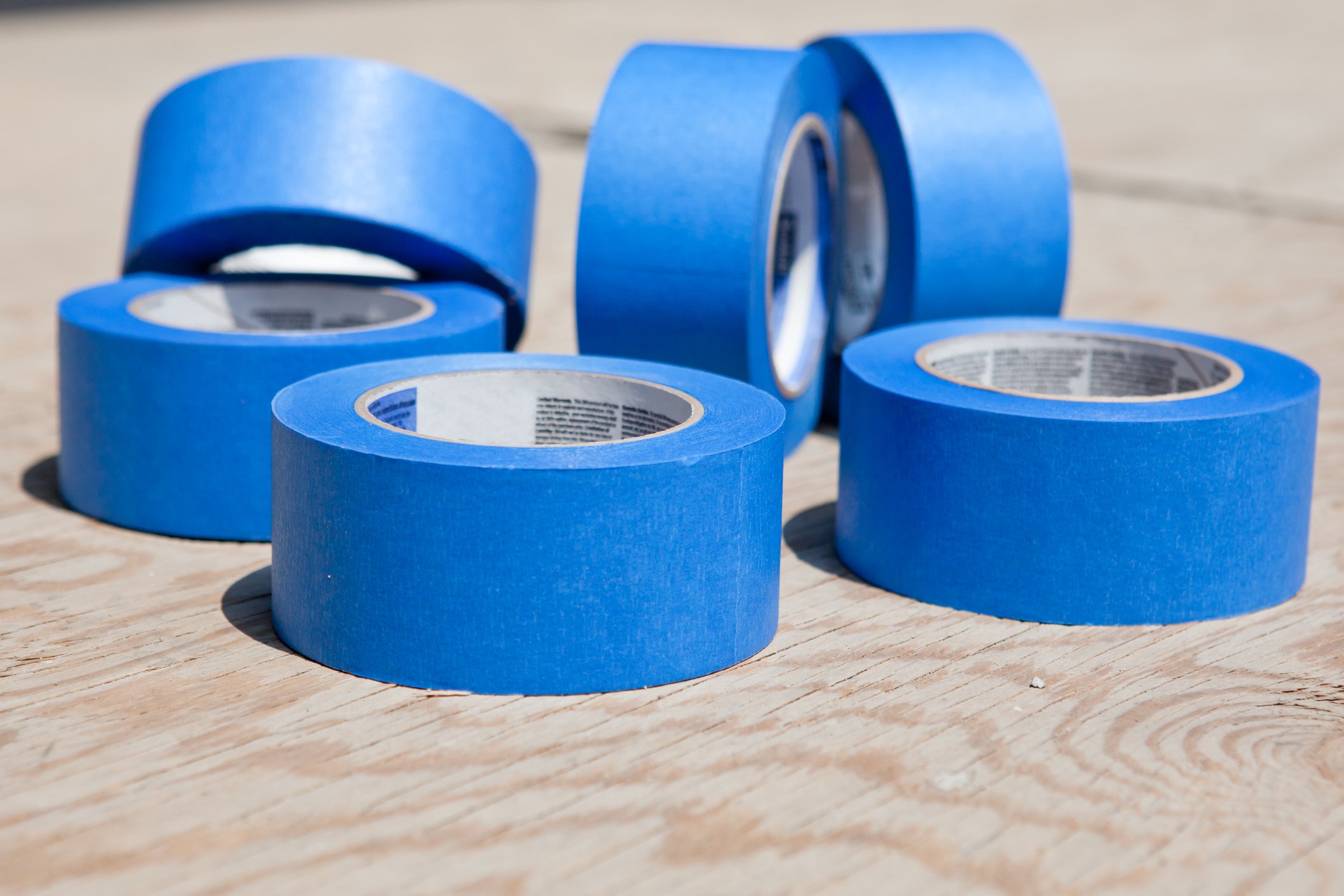 Six rolls of blue tape on a wooden table. 