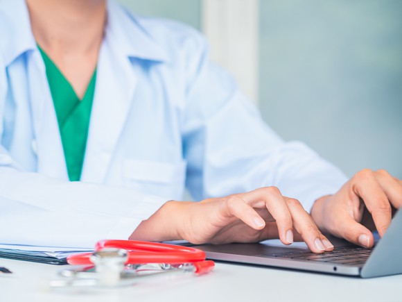 Person in lab coat typing on a laptop. 