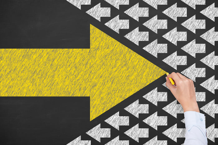 A large yellow arrow going against a sea of white arrows facing the opposite direction.