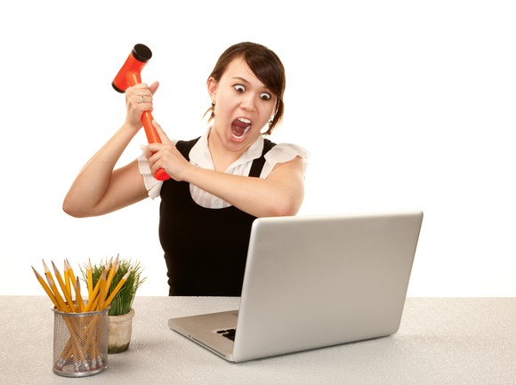 Businesswoman screaming and swinging an orange mallet at her laptop.