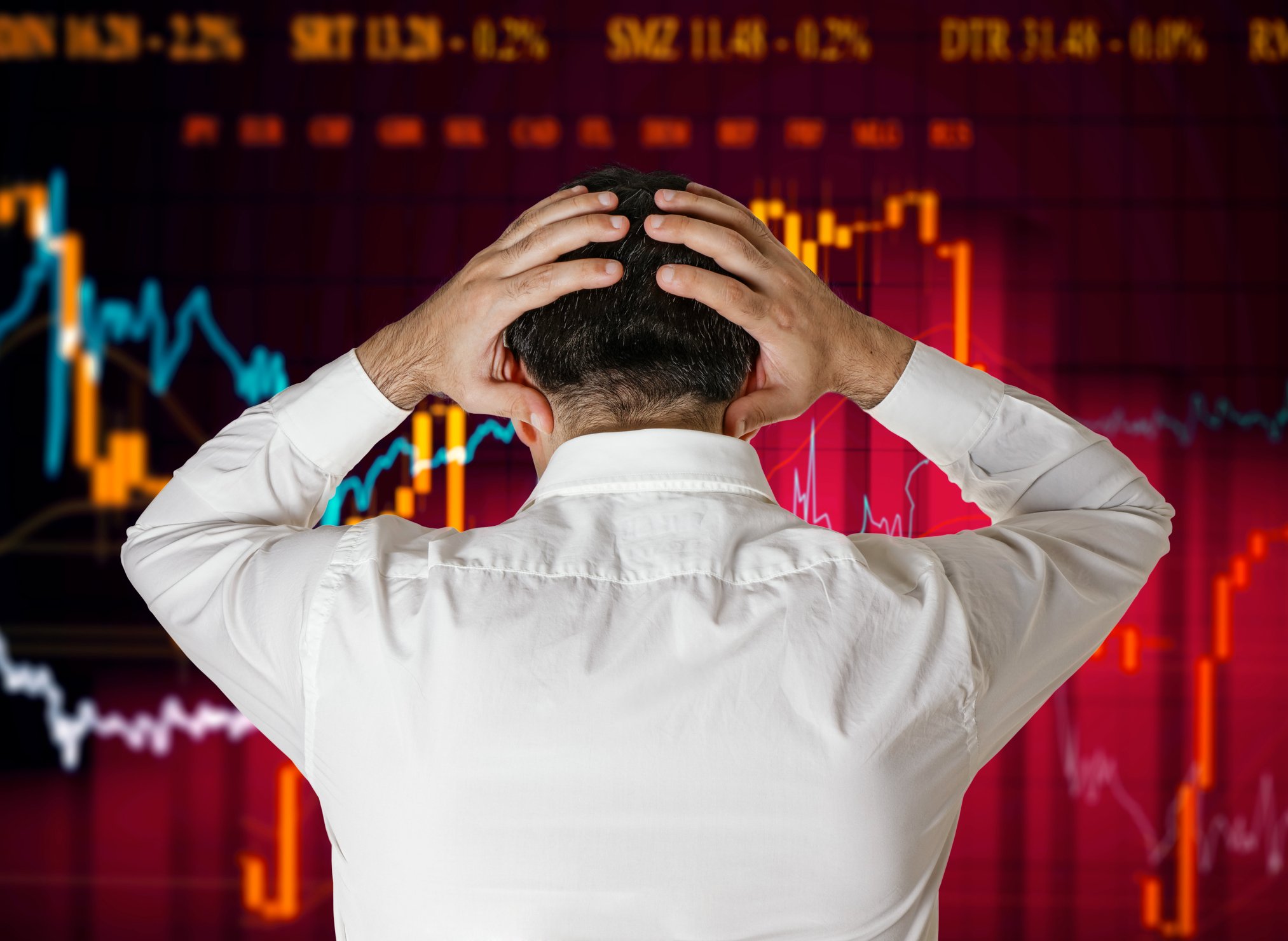 Businessman with hands on head in frustration while looking at stock charts.