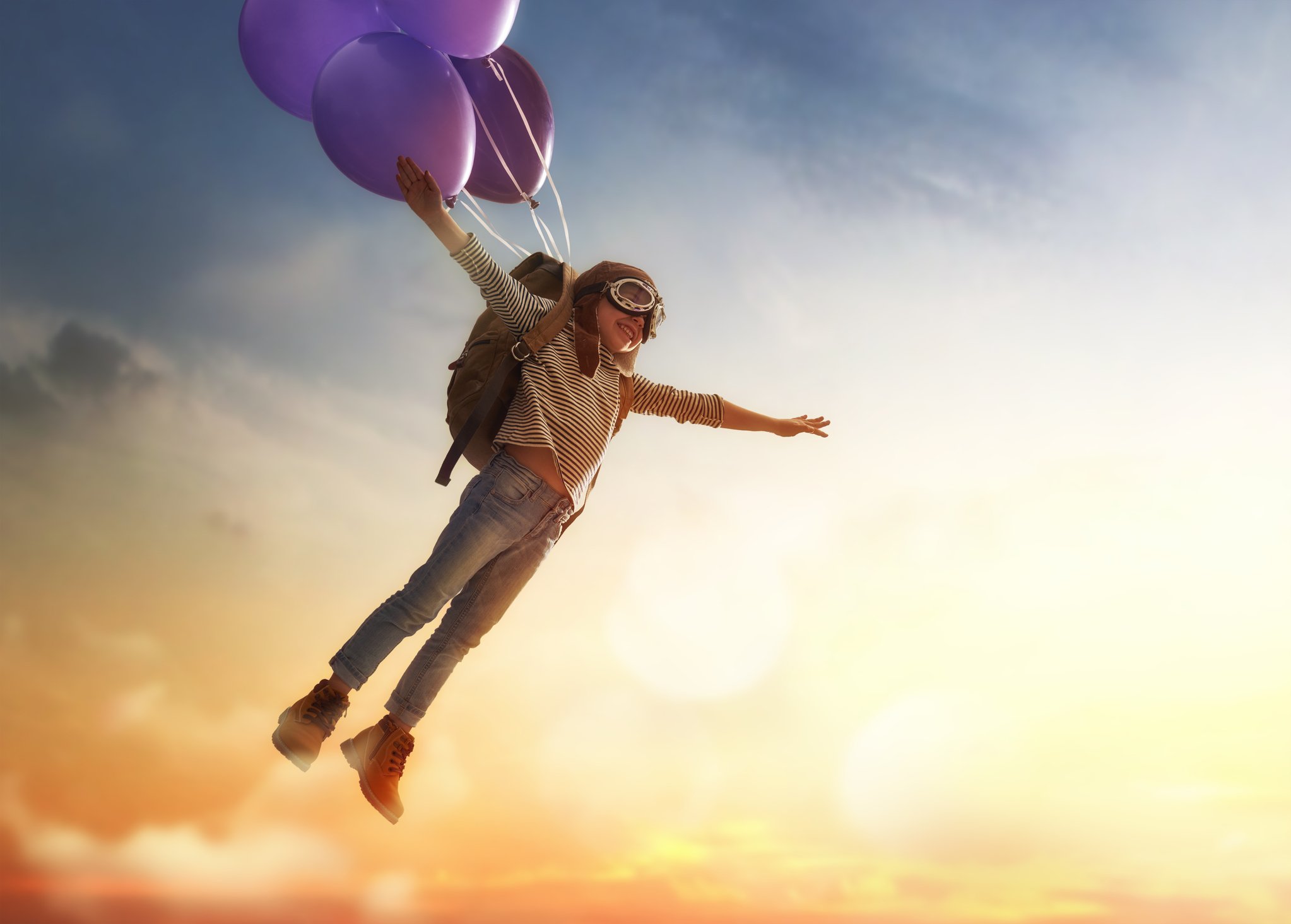 With purple balloons attached to his backpack, a child, dressed as an aviator, flies through the air.
