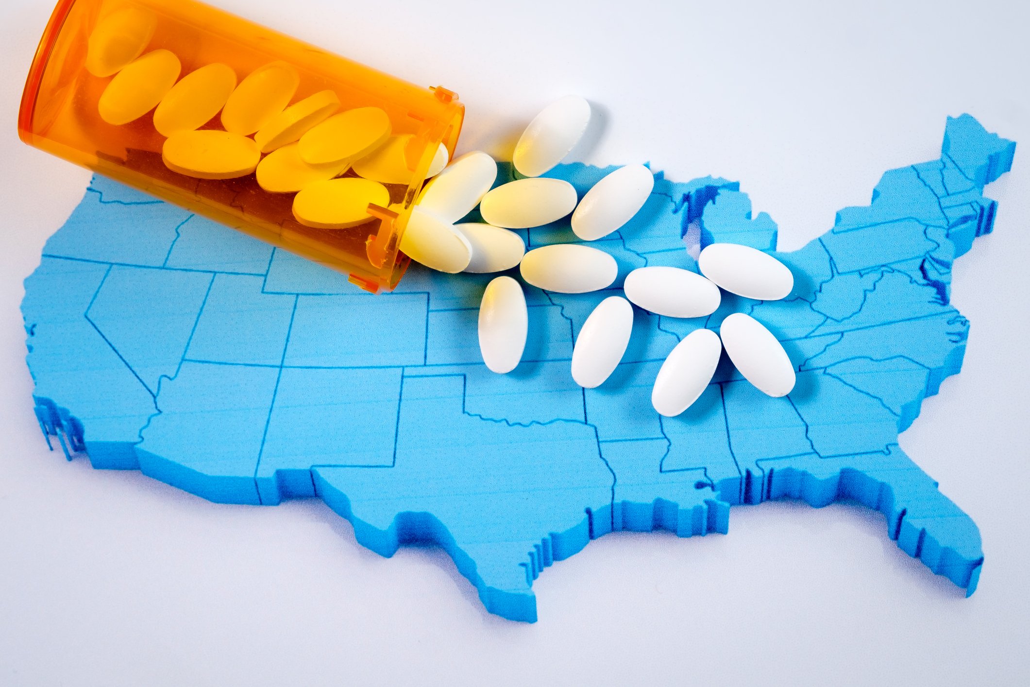 Translucent orange bottle spilling pills on top of a raised blue U.S. map