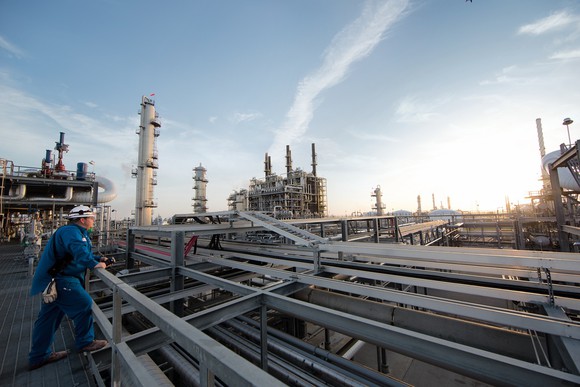 Worker in hard hat looking over a network of pipes and processing equipment for energy products.