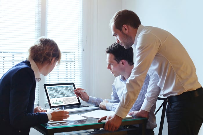 Workers gather around a computer.