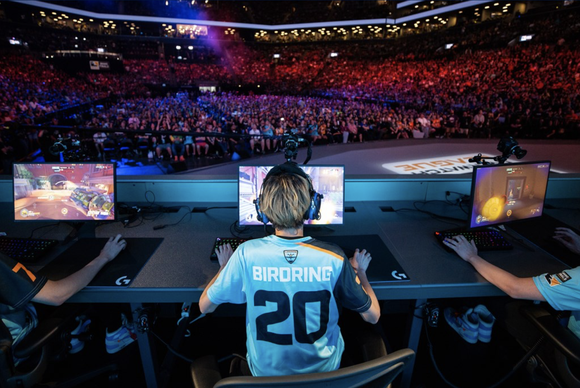 Professional esport player on a stage competing in front of a large audience in an arena.
