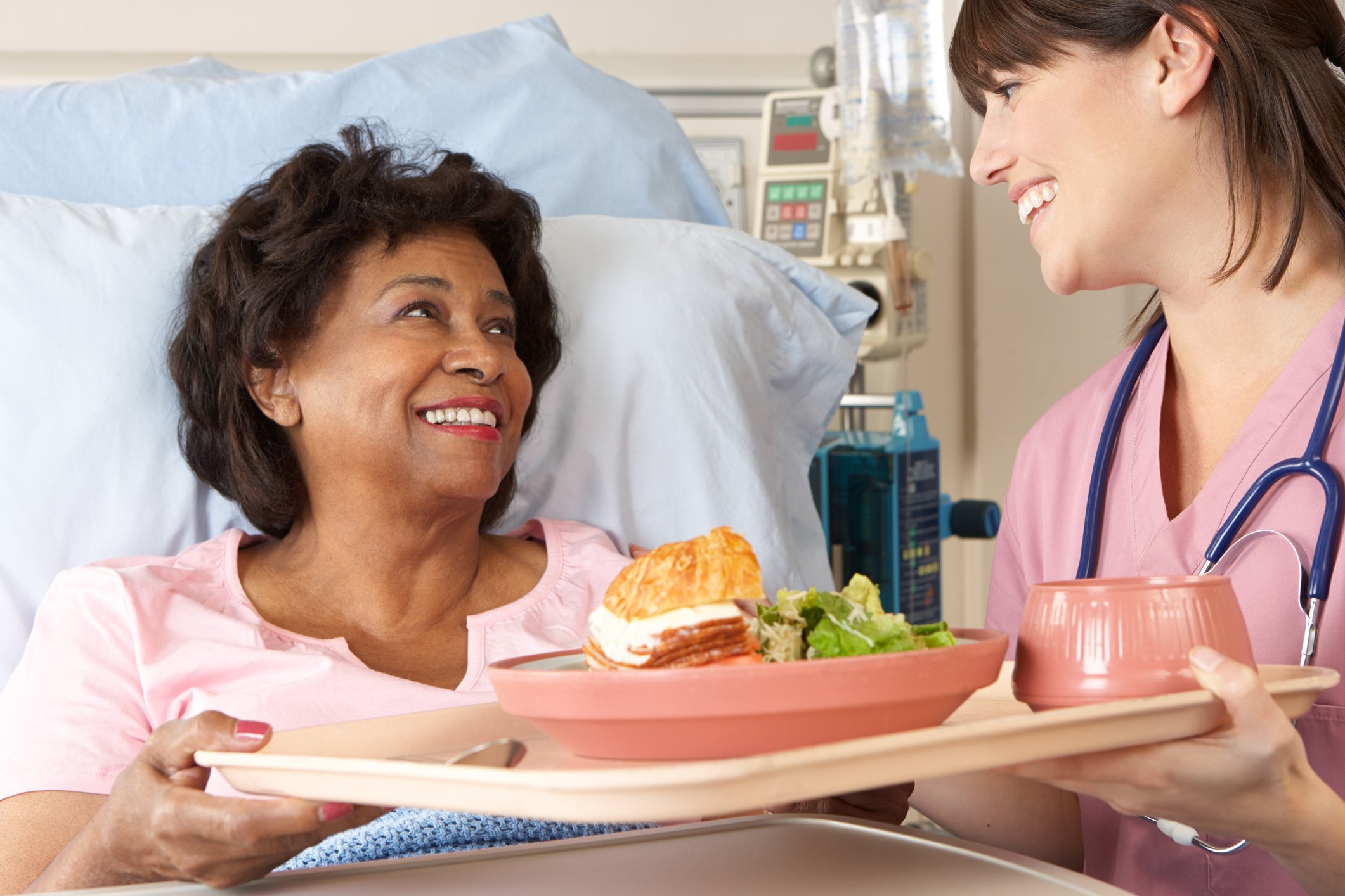 Nurse delivering food to an older woman in a hospital bed
