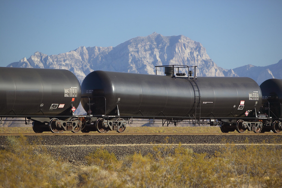 Three tanker cars on a railroad track in front of a mountain view.
