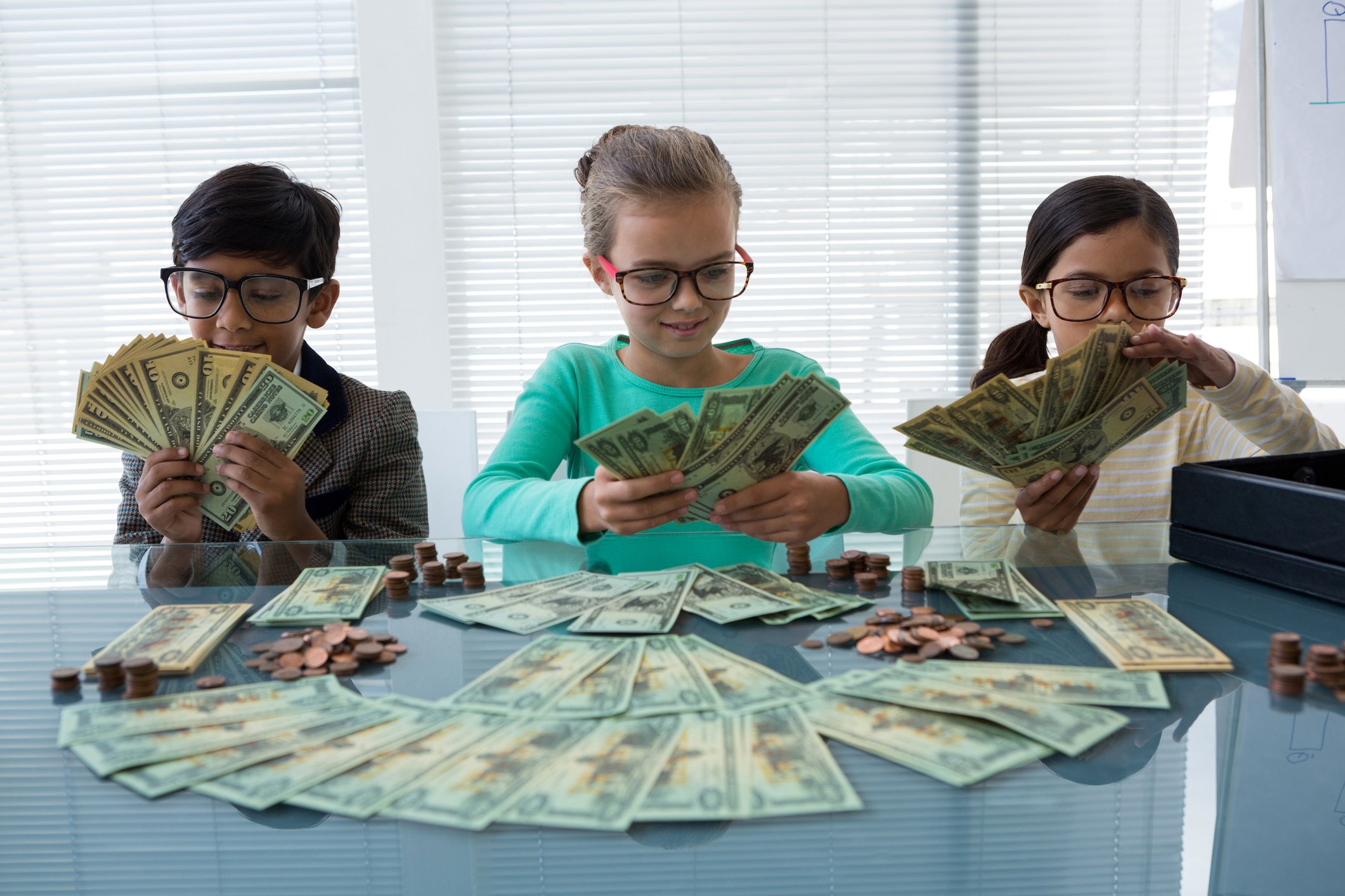 Three bespectacled pre-teens inspecting wads of cash and smiling
