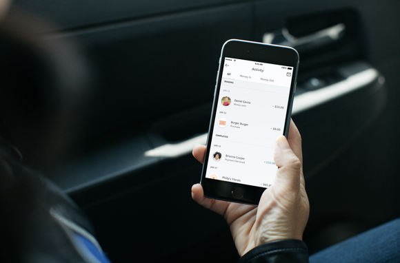 A man's hand holding a smartphone with the PayPal app displayed.