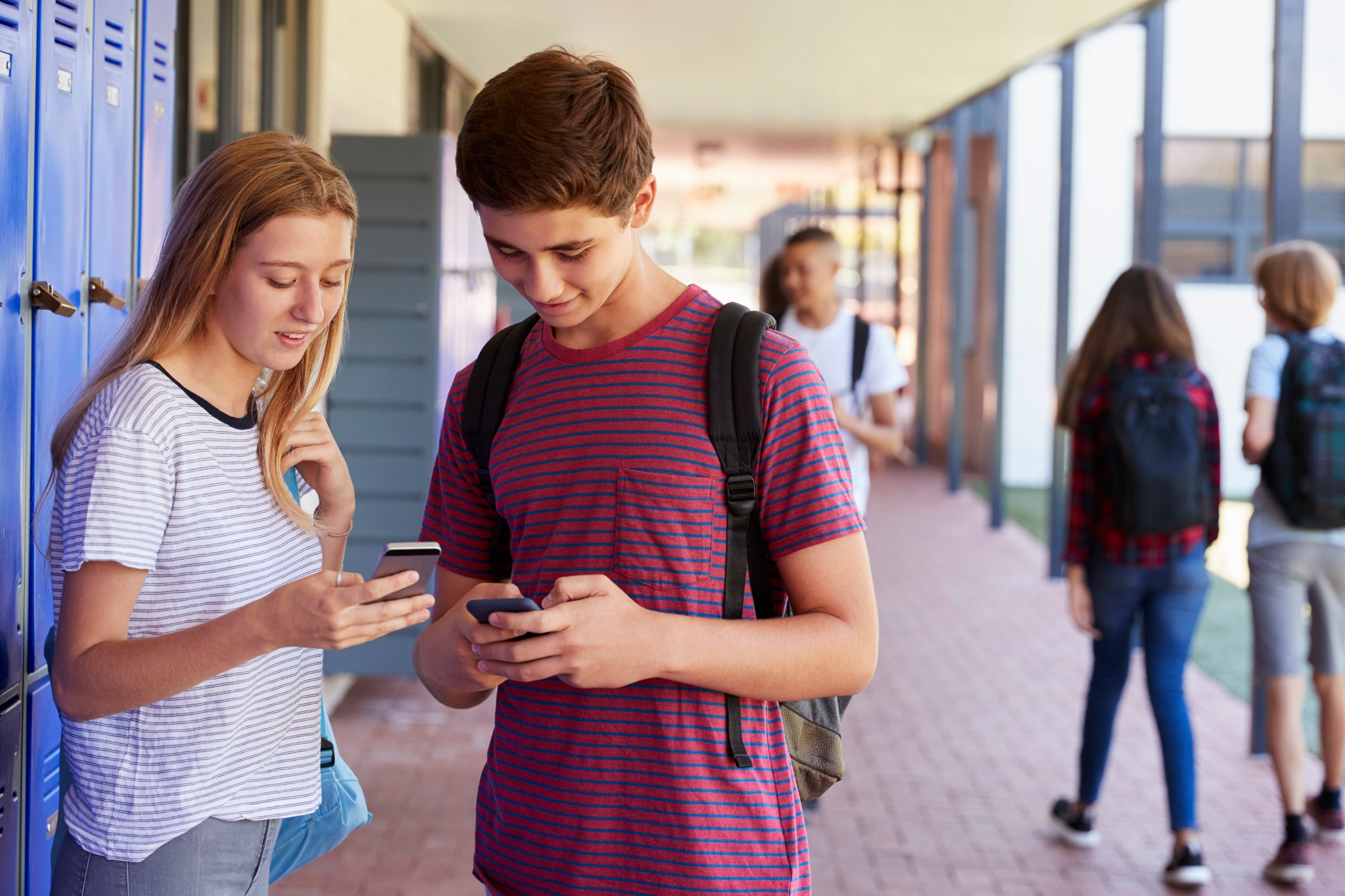 Teens looking at their phones by school lockers.
