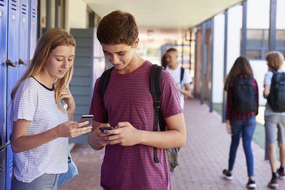 Teens looking at their phones by school lockers.